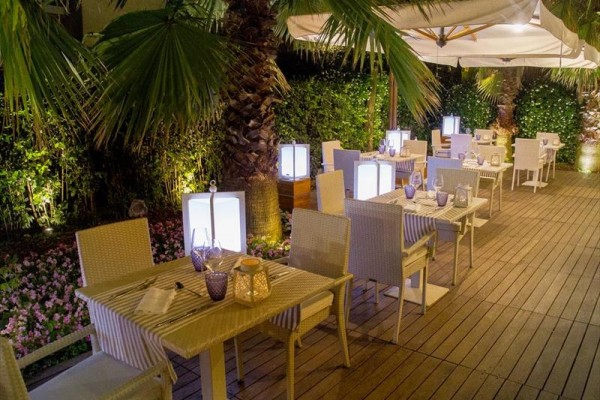 Zewnętrzna restauracja z nakrytymi stołami, otoczona palmami i oświetlona lampami.