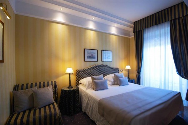 Elegancki pokój hotelowy z łóżkiem małżeńskim, lampami i zasłonami.