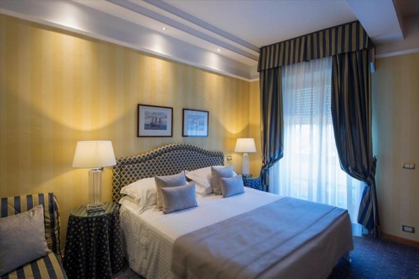 Luksusowy pokój hotelowy z łóżkiem małżeńskim, lampami i dużym oknem z zasłoną.