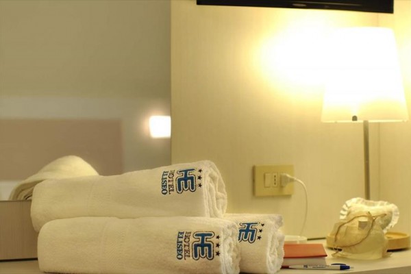Białe ręczniki z logo hotelu obok zapalonej lampy na stole.