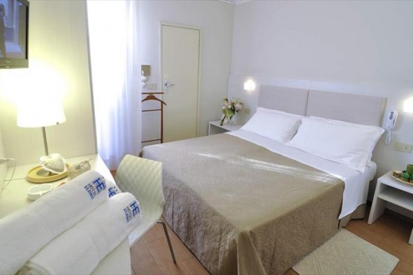 Jasny pokój hotelowy z podwójnym łóżkiem i telewizorem.