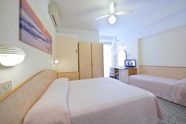 Pokój hotelowy z dwoma łóżkami, telewizorem i meblami w jasnych kolorach.