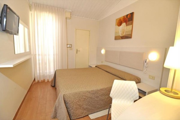 Nowoczesny pokój hotelowy z podwójnym łóżkiem, lampą i telewizorem na ścianie.