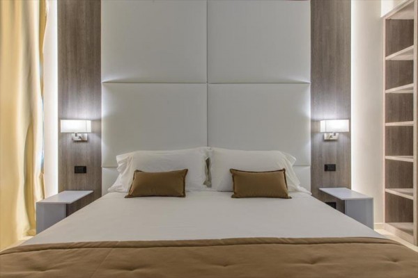 Nowoczesna sypialnia hotelowa z łóżkiem małżeńskim i jasnymi zasłonami.