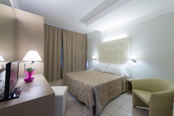 Nowoczesny pokój hotelowy z podwójnym łóżkiem, fotelem, biurkiem i lampami.