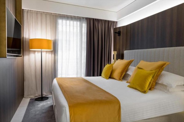 Nowoczesny pokój hotelowy z podwójnym łóżkiem, żółtymi poduszkami i lampą przy oknie.
