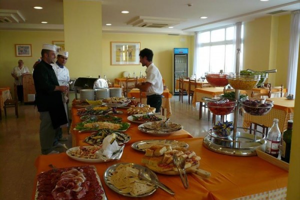 Restauracja hotelowa z bufetem pełnym różnych potraw i kucharzami w tle.