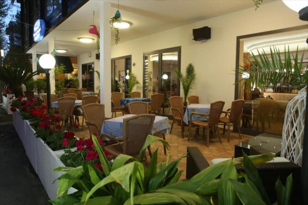 Zewnętrzny taras restauracji z wiklinowymi krzesłami i kwiatami.