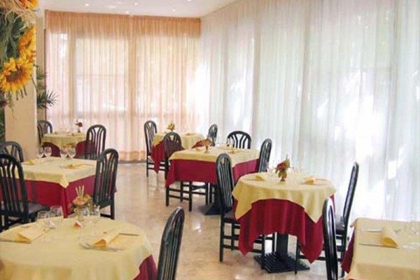Restauracja z okrągłymi stołami pokrytymi żółtymi obrusami i krzesłami wokół.  