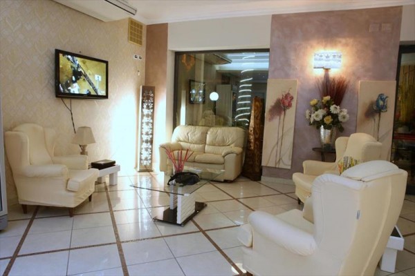 Elegancki salon z kremowymi fotelami i sofą, ozdobiony obrazami kwiatowymi i telewizorem na ścianie.