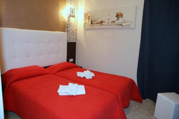Dwa pojedyncze łóżka z czerwoną pościelą i złożonymi ręcznikami w pokoju hotelowym.