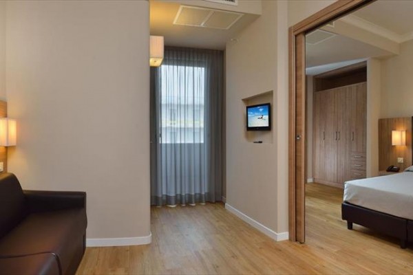 Nowoczesny pokój hotelowy z łóżkiem małżeńskim, sofą i telewizorem na ścianie.