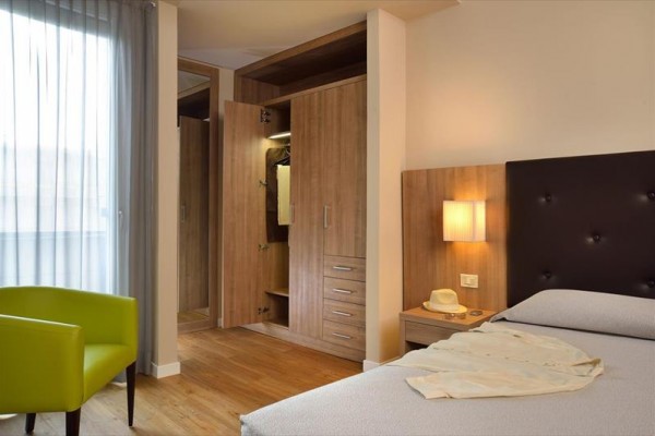 Nowoczesny pokój hotelowy z otwartą szafą, łóżkiem i zielonym fotelem.