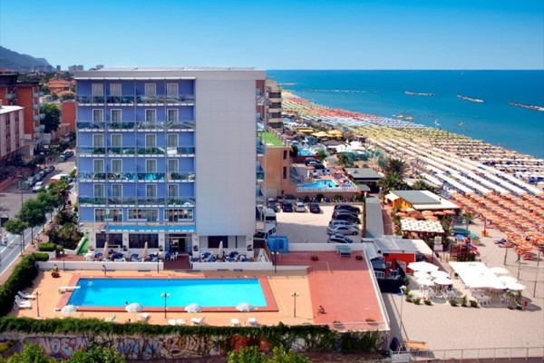 Hotel przy plaży z basenem zewnętrznym i parasolami.