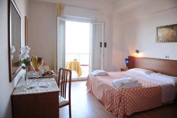 Jasny pokój hotelowy z łóżkiem małżeńskim i balkonem.