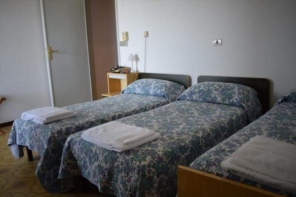Trzy pojedyncze łóżka z kwiecistą narzutą i ręcznikami w rzędzie.