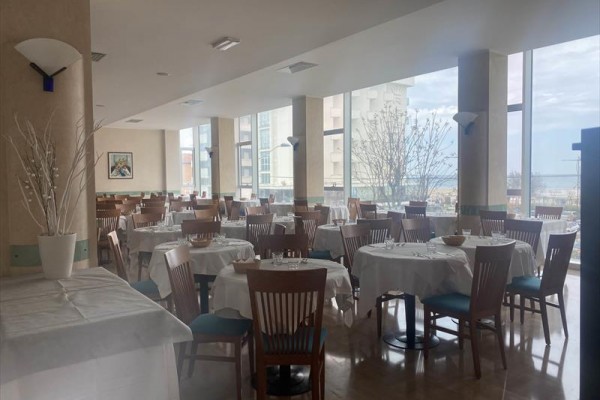 Restauracja z okrągłymi stołami i drewnianymi krzesłami przy dużych oknach z widokiem.