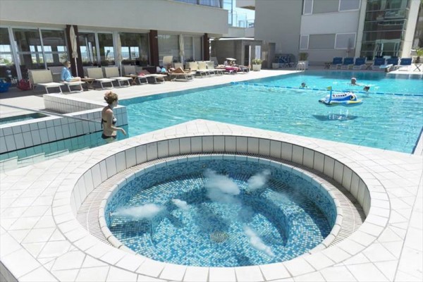 Jacuzzi i basen przy nowoczesnym hotelu z leżakami.