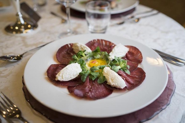 Talerz z carpaccio, serem i warzywami ułożonymi na białej porcelanie.