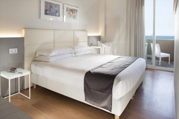 Nowoczesny pokój hotelowy z dużym łóżkiem i balkonem z widokiem na morze.