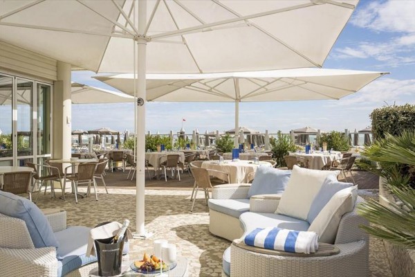 Zewnętrzny taras restauracji z parasolami i wygodnymi fotelami przy plaży.
