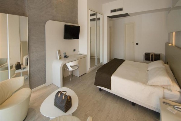 Nowocześnie urządzony pokój hotelowy z podwójnym łóżkiem, biurkiem i fotelami.