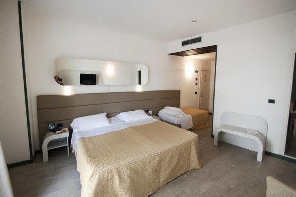 Pokój hotelowy z dwoma łóżkami, stolikami nocnymi i lustrem nad zagłówkiem.
