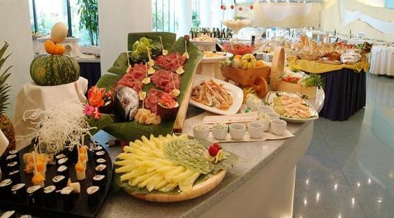 Bufetowy stół z różnorodnymi potrawami, w tym sushi, owocami i mięsem.