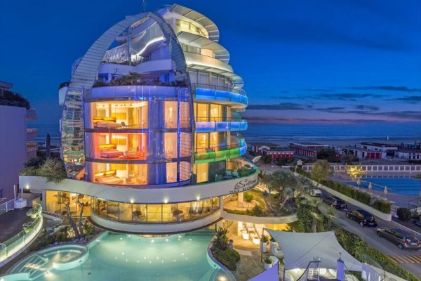 Nowoczesny hotel z kolorowym oświetleniem wieczornym i basenem na pierwszym planie.
