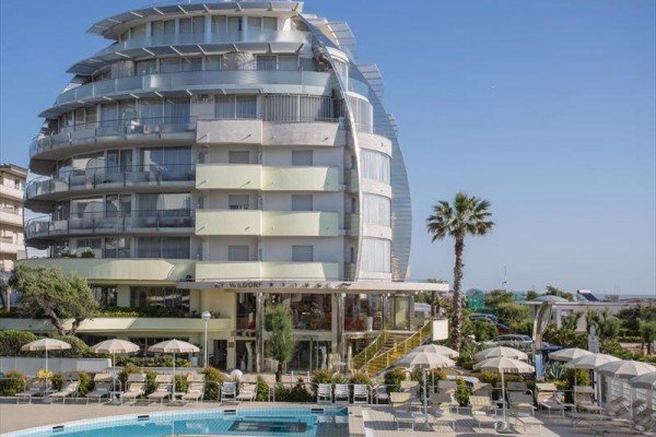 Nowoczesny hotel z basenem i leżakami na zewnątrz pod parasolami.