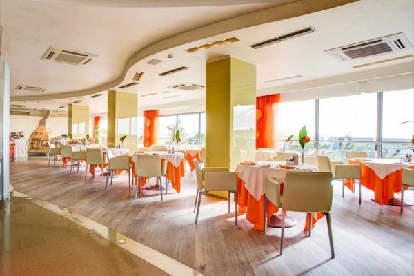 Wnętrze jasnej nowoczesnej restauracji z pomarańczowymi obrusami i dużymi oknami.