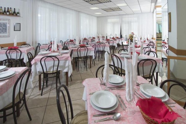 Restauracja z wieloma stołami przykrytymi różowymi obrusami i białymi serwetkami.