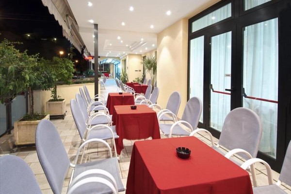 Taras restauracji z czerwonymi obrusami na stołach i białymi krzesłami.