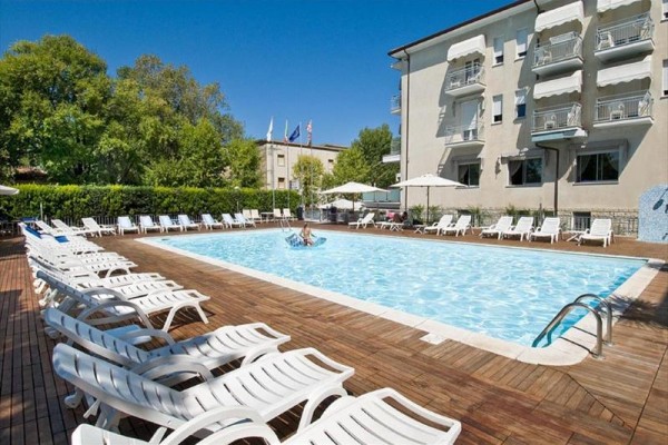 Na zewnątrz znajduje się basen otoczony leżakami przy wielopiętrowym hotelu.