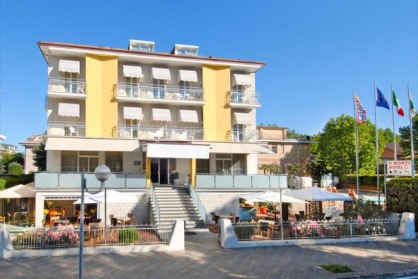Czteropiętrowy hotel z żółtymi balkonami i parasolami przed wejściem.