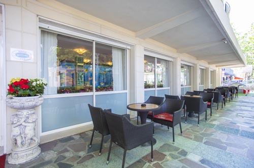 Zewnętrzne miejsca siedzące restauracji z czarnymi krzesłami i okrągłymi stolikami przy dużych oknach.