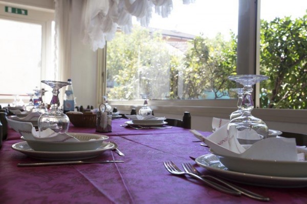 Stół w restauracji, nakryty fioletowym obrusem, talerzami i kieliszkami.