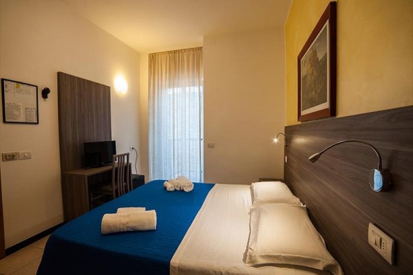 Pokój hotelowy z łóżkiem małżeńskim, biurkiem i zasłonami przy oknie.  
