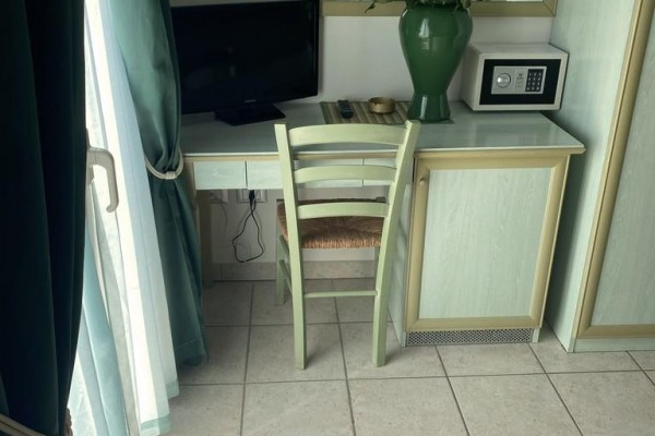 Stół z krzesłem, monitorem komputerowym i wazonem z kwiatami przy oknie.