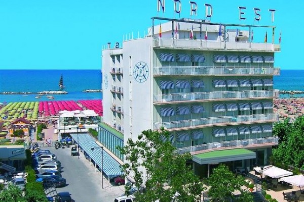 Hotel Nord Est przy plaży z kolorowymi parasolami i niebieskim niebem w tle.