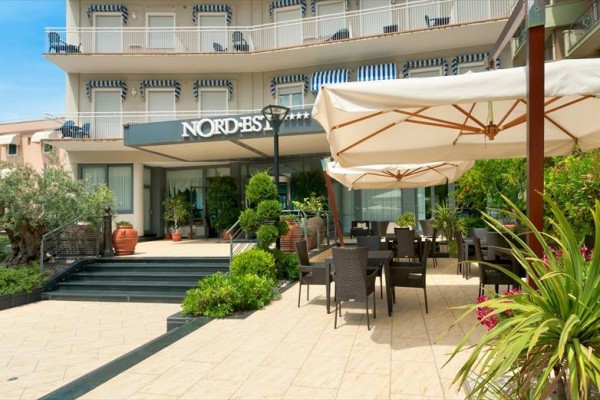 Zewnętrze hotelu ze stolikami i parasolami na tarasie.
