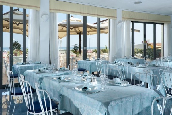Restauracja z niebieskimi obrusami i widokiem na taras z parasolami.