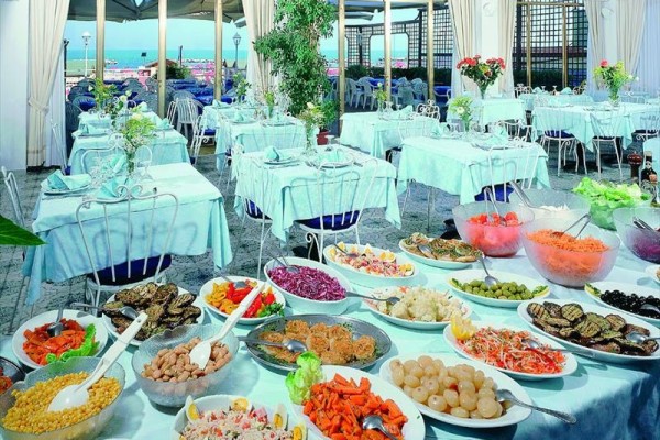 Ustawienie stołów z bufetem pełnym różnorodnych potraw w restauracji z widokiem na zewnętrzny taras.