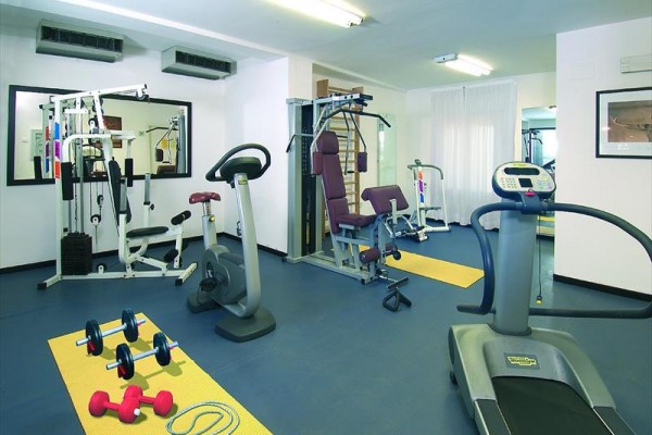 Siłownia z różnorodnym sprzętem fitness, w tym bieżnią i hantlami.