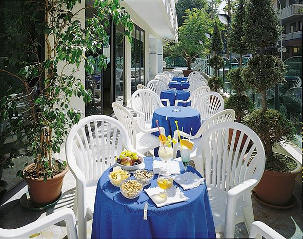 Restauracyjny taras z niebieskimi obrusami, białymi krzesłami i jedzeniem na stołach.