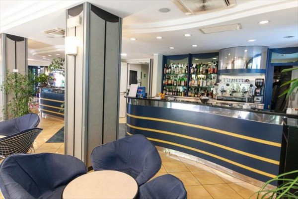 Nowoczesny hotelowy bar z niebieskimi fotelami i półkami z napojami.
