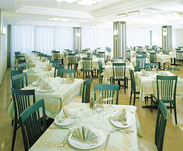 Restauracja z nakrytymi stołami i zielonymi krzesłami.