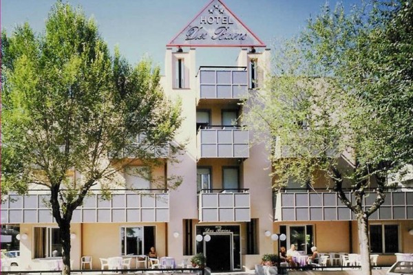 Fasada hotelu otoczona drzewami z zewnętrznymi stolikami i krzesłami.