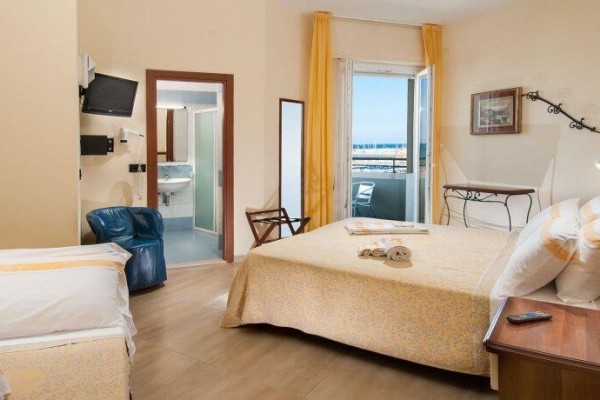 Jasny pokój hotelowy z łóżkiem małżeńskim, pojedynczym łóżkiem i widokiem na morze.
