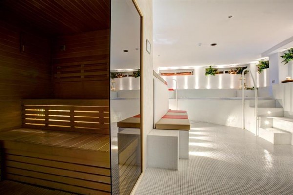 Nowoczesna przestrzeń wellness z drewnianą sauną i białymi elementami ceramicznymi.